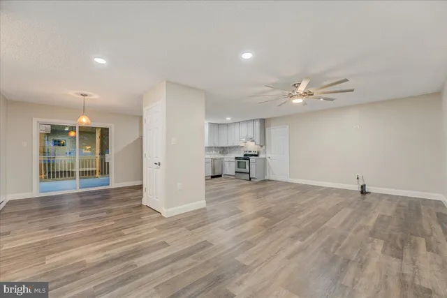 a view of empty room with wooden floor and kitchen