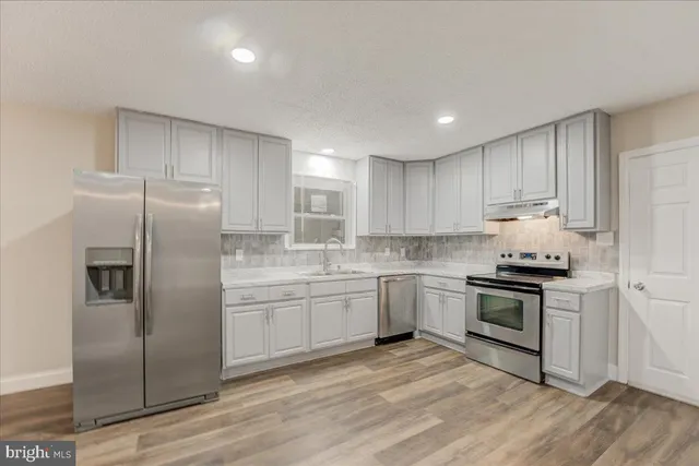 a kitchen with stainless steel appliances granite countertop a stove a sink dishwasher a refrigerator and white cabinets with wooden floor