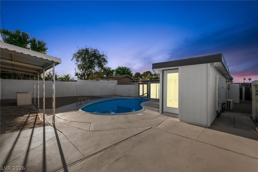 Pool at dusk featuring a patio, a fenced backyard, and an outdoor structure