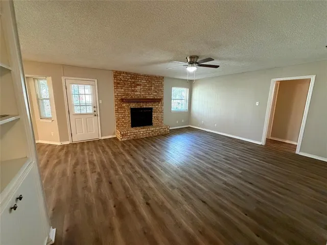 an empty room with wooden floor fireplace and windows
