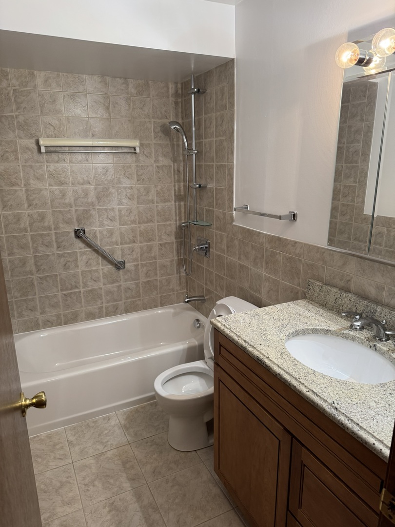 9244 Gross Point Road, Unit 103 Skokie, IL 60077 - Photo 12 of 28 a bathroom with a granite countertop bathtub shower sink vanity and toilet