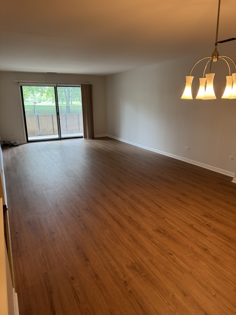 9244 Gross Point Road, Unit 103 Skokie, IL 60077 - Photo 5 of 28 an empty room with wooden floor and windows