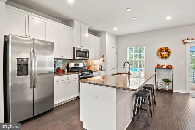 a kitchen with stainless steel appliances granite countertop a refrigerator a stove top oven a dining table and chairs with wooden floor