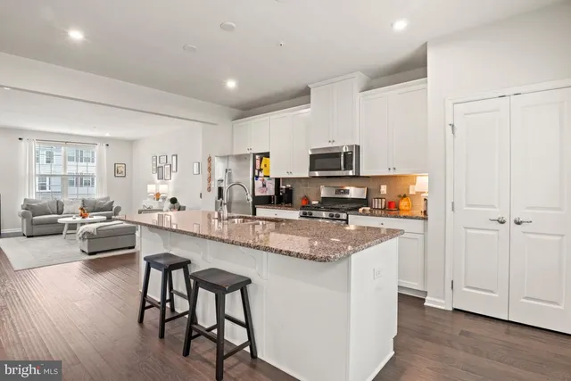 a kitchen with stainless steel appliances granite countertop a stove top oven a sink dishwasher a dining table and chairs with wooden floor