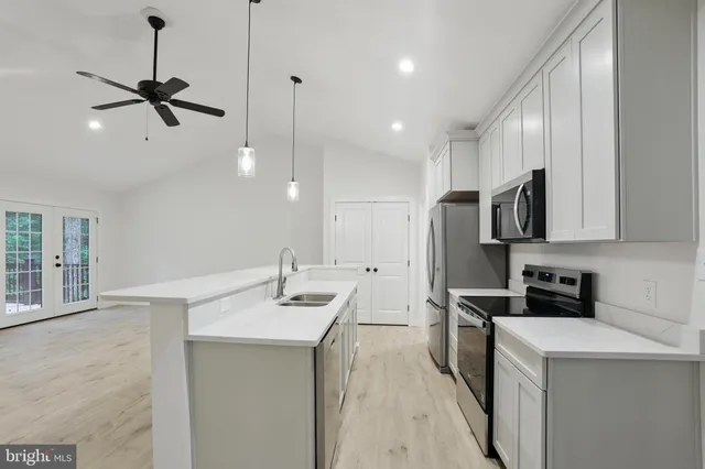 a kitchen with stainless steel appliances a sink dishwasher a refrigerator and white cabinets with wooden floor