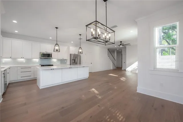 a large kitchen with stainless steel appliances kitchen island granite countertop a stove a sink a center island a refrigerator and a wooden floor