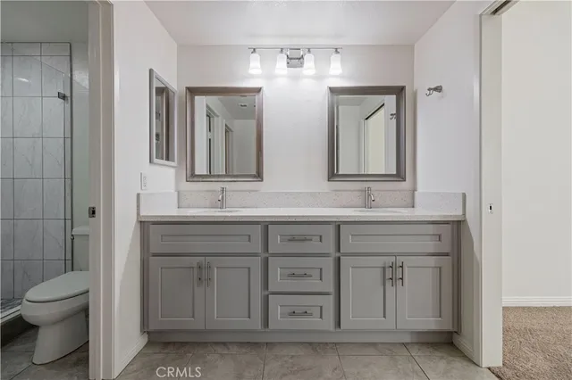 a bathroom with a granite countertop double vanity sink a mirror and a toilet