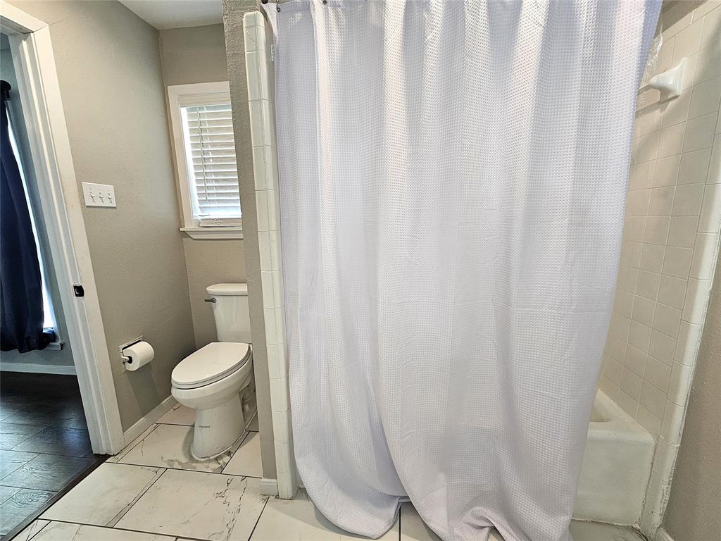1205 West Trinity Street Groesbeck, TX 76642 - Photo 17 of 28 a bathroom with a toilet and a shower curtain