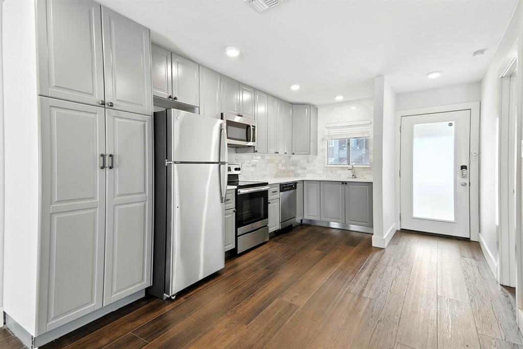 909 Reinli Street, Unit 144 Austin, TX 78751 - Photo 5 of 19 Kitchen featuring stainless steel appliances, decorative backsplash, dark wood-style floors, light countertops, and gray cabinets