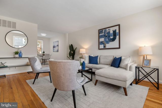 a living room with furniture a lamp paintings and a wooden floor