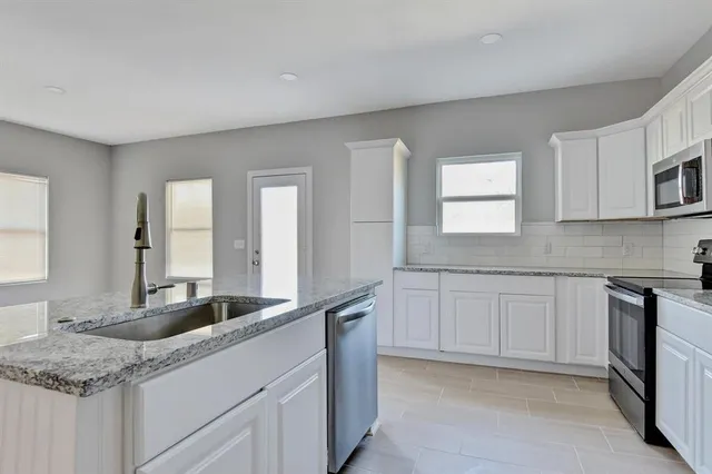 a kitchen with granite countertop white cabinets white appliances a sink and a window