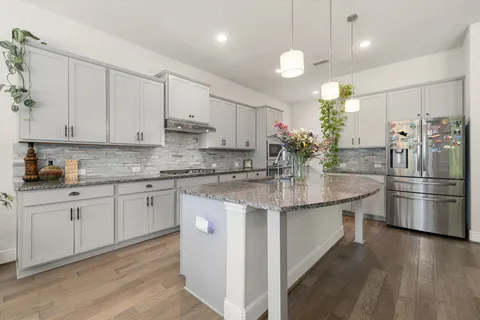 a kitchen with stainless steel appliances granite countertop a sink a stove a refrigerator and island with wooden floor