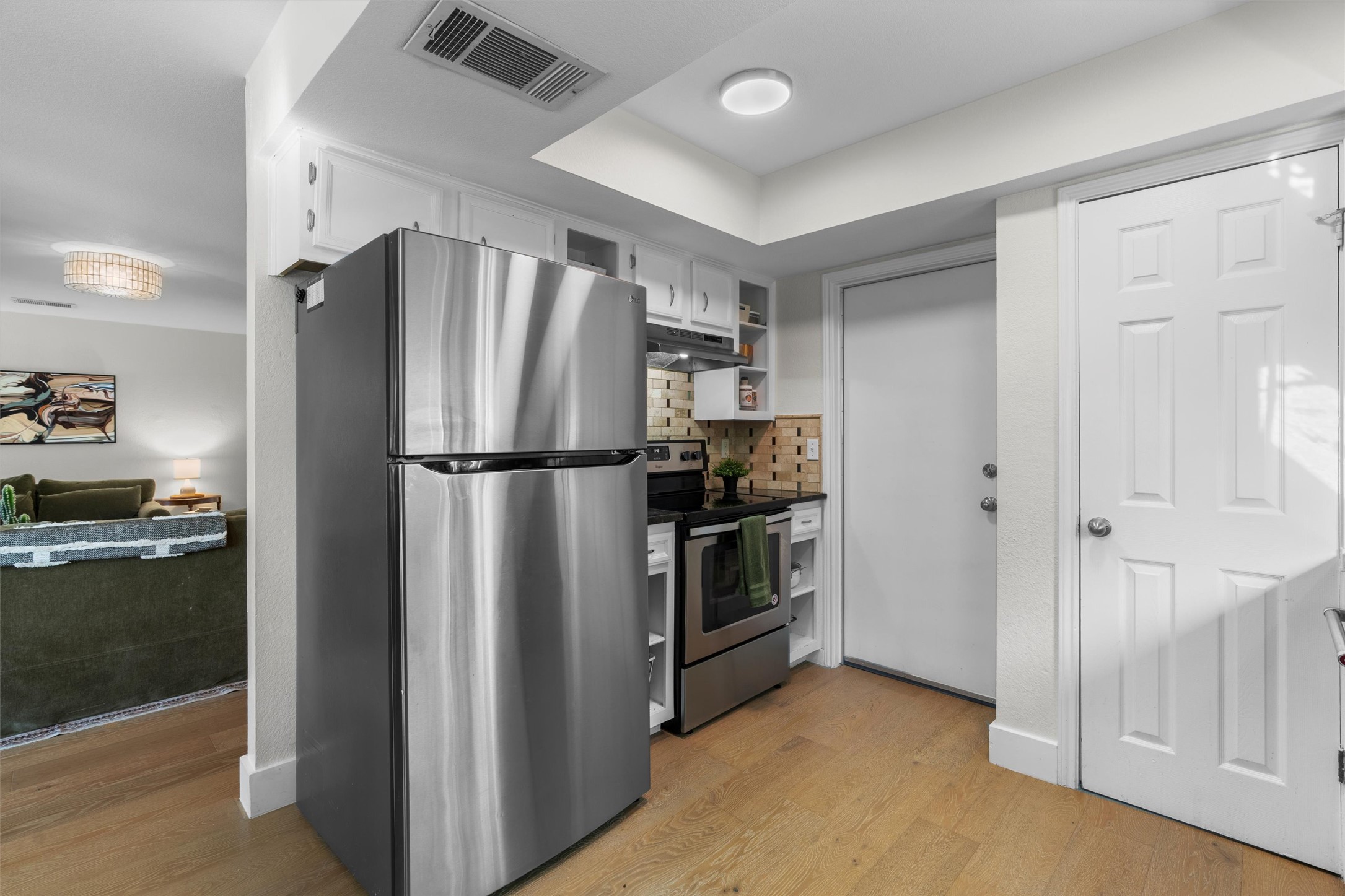 3431 Bliss Spillar Road Manchaca, TX 78652 - Photo 10 of 30 Kitchen featuring stainless steel appliances, dark countertops, light wood-style flooring, white cabinetry, and backsplash
