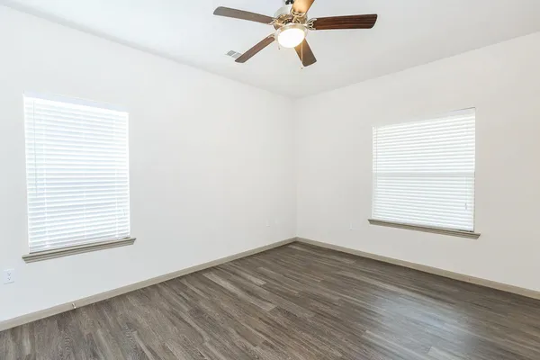 an empty room with wooden floor windows and fan