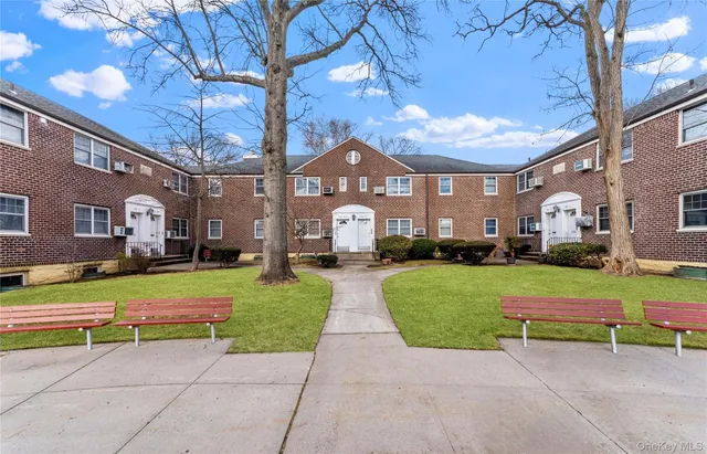a front view of a building with garden and trees