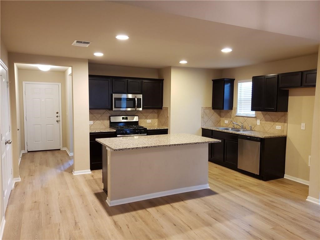 14909 Custis Lane Austin, TX 78725 - Photo 5 of 21 a kitchen with stainless steel appliances kitchen island granite countertop a stove a sink and a refrigerator