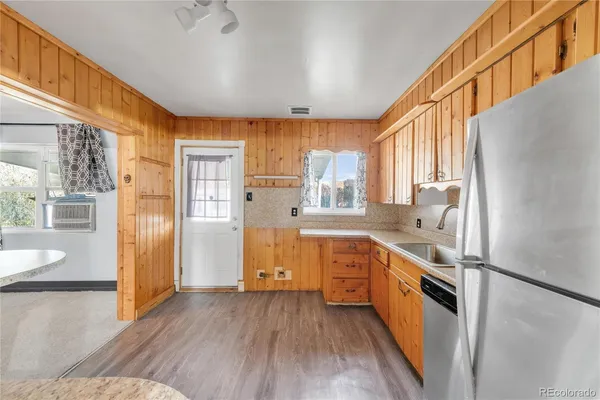 a kitchen with stainless steel appliances granite countertop a refrigerator a sink dishwasher a stove and white countertops with wooden floor