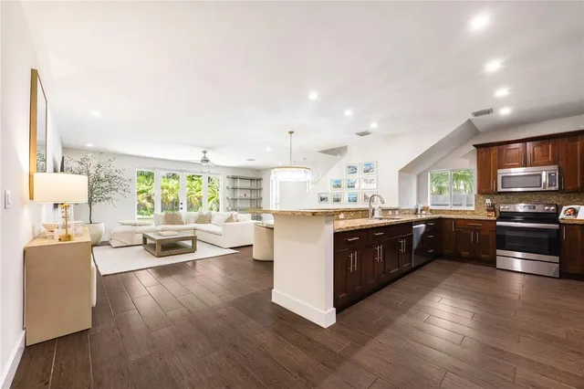 a kitchen with stainless steel appliances kitchen island granite countertop a stove top oven a sink a dining table and chairs with wooden floor