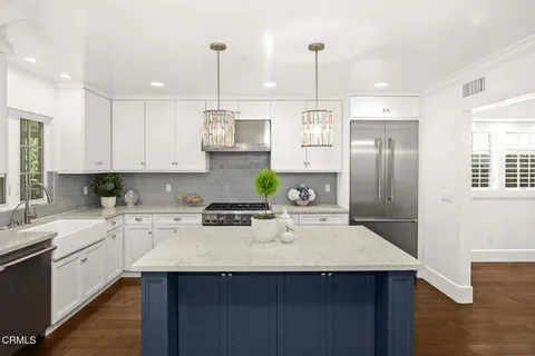 a kitchen with stainless steel appliances granite countertop a sink a stove a refrigerator and white cabinets