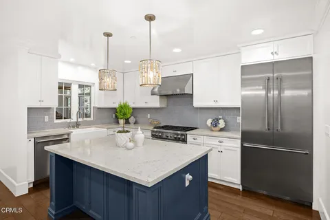 a kitchen with stainless steel appliances kitchen island a refrigerator a sink a stove and white cabinets