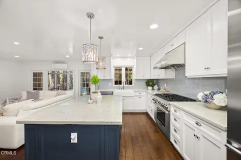 a kitchen with stainless steel appliances kitchen island granite countertop a stove a sink dishwasher and white cabinets with wooden floor