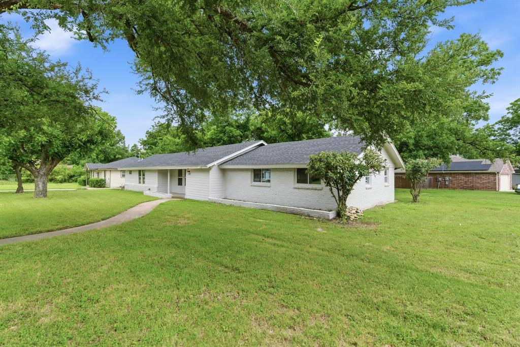 507 Country Club Road Cleburne, TX 76033 - Photo 3 of 39 Ranch-style exterior with white painted brick and siding, featuring a dark shingle roof, a concrete walkway, and established trees