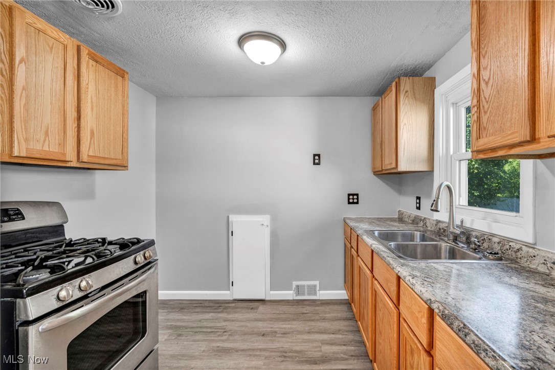 1135 Keefer Road Girard, OH 44420 - Photo 5 of 32 Kitchen with stainless steel gas range, light wood-style floors, a textured ceiling, and light countertops