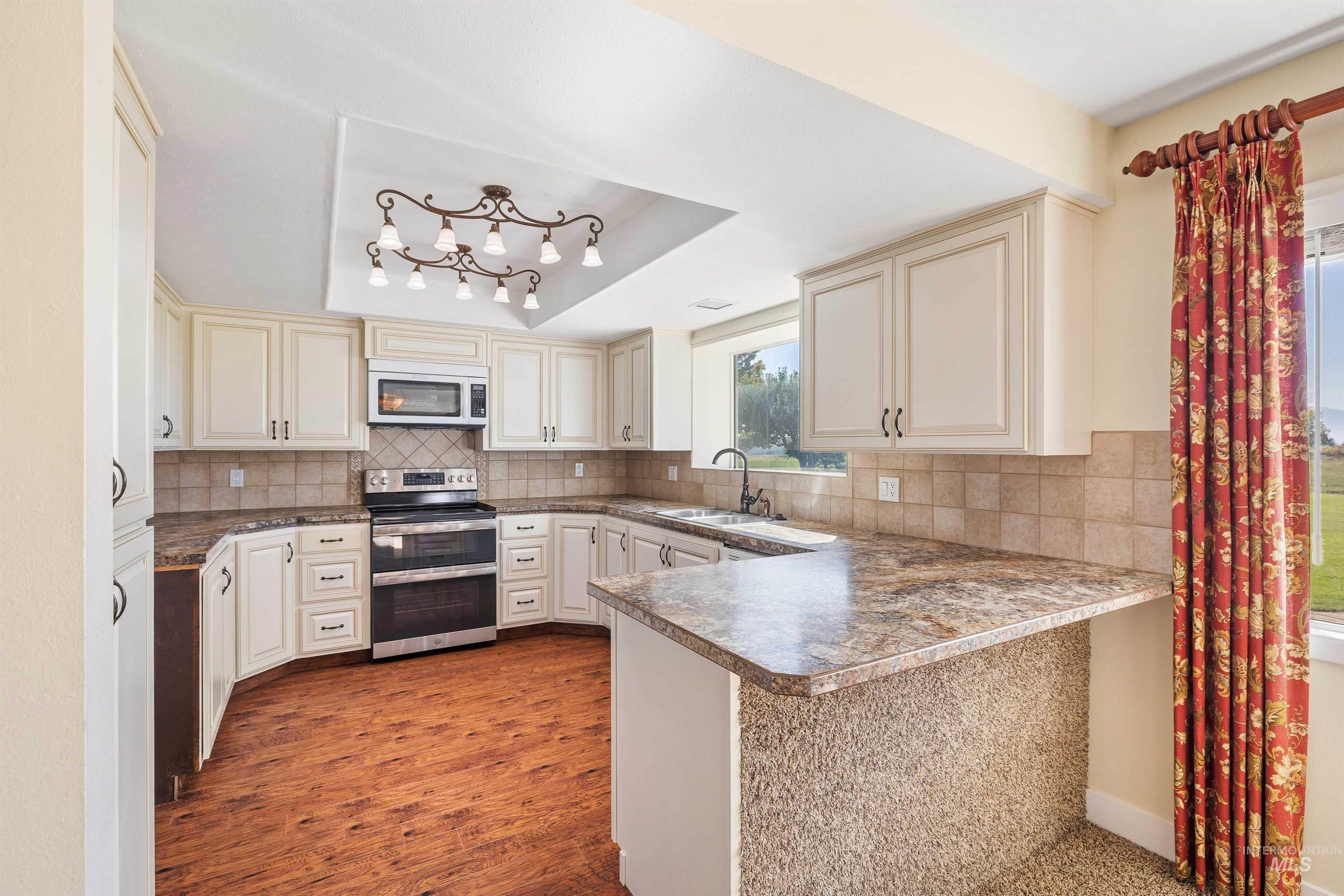 415 West 300 South Heyburn, ID 83336 - Photo 10 of 50 Kitchen with decorative backsplash, a peninsula, a tray ceiling, double oven range, and dark wood finished floors