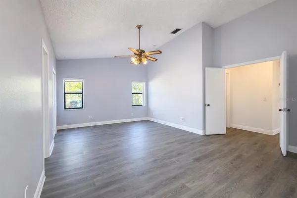an empty room with wooden floor chandelier fan and windows