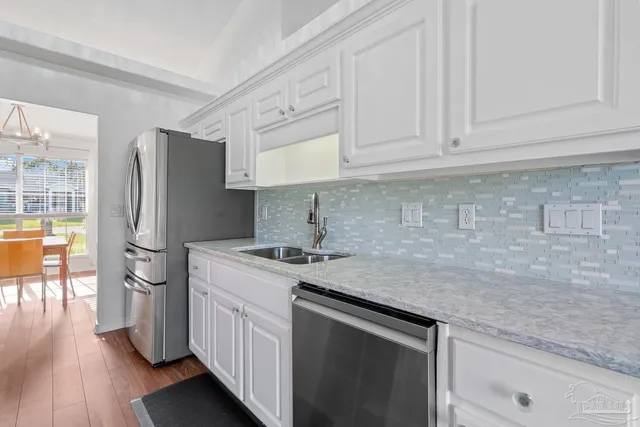 a kitchen with stainless steel appliances granite countertop a refrigerator a sink dishwasher a stove and white cabinets with wooden floor