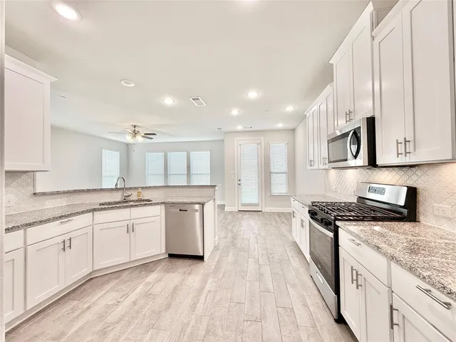 a large kitchen with granite countertop a stove top oven a sink dishwasher and white cabinets with wooden floor