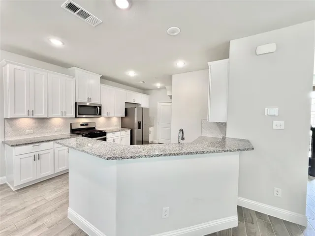 a kitchen with stainless steel appliances granite countertop a sink a stove a refrigerator and white cabinets