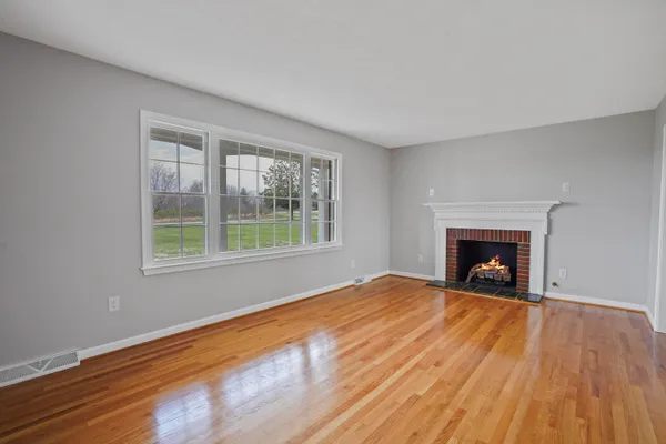 a view of an empty room with wooden floor fireplace and a window