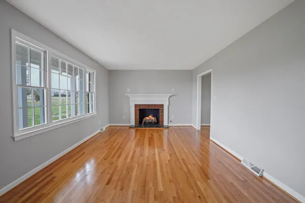 a view of an empty room with wooden floor fireplace and a window