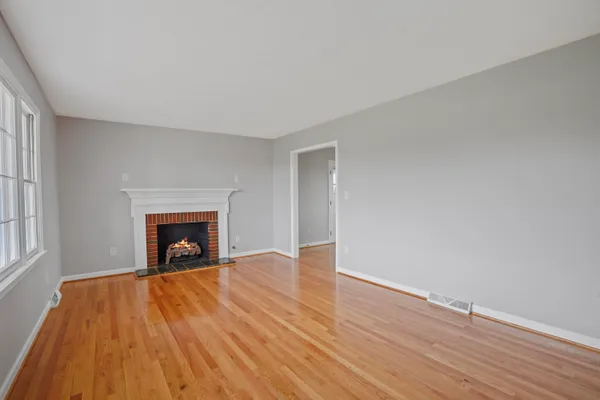 a view of an empty room with wooden floor fireplace and a window