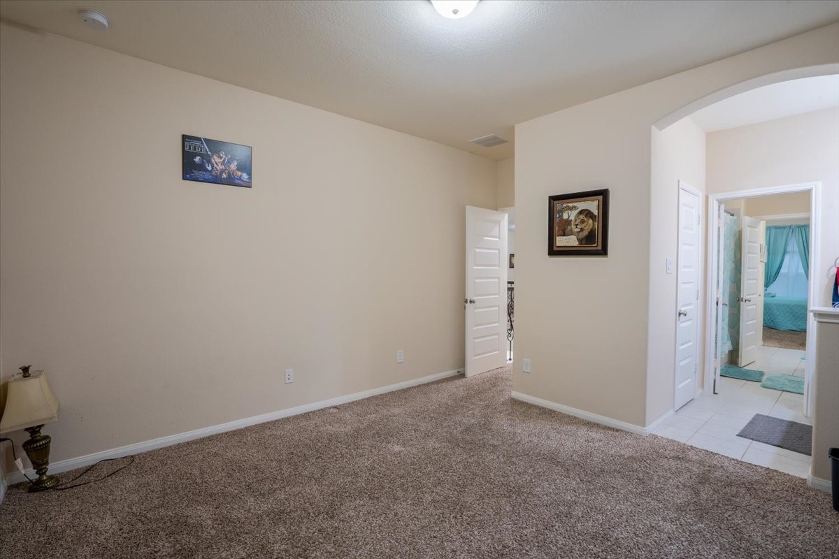 22002 Flashing Ridge Spring, TX 77389 - Photo 29 of 43 This photo shows a cozy room with neutral walls and carpeted flooring. It features an arched doorway leading to a tiled area, possibly a bathroom, with visible teal accents. The space is well-lit, with a simple, clean design.