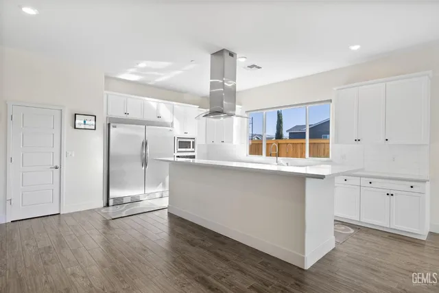 a kitchen with stainless steel appliances granite countertop a refrigerator a sink dishwasher a stove and white cabinets with wooden floor