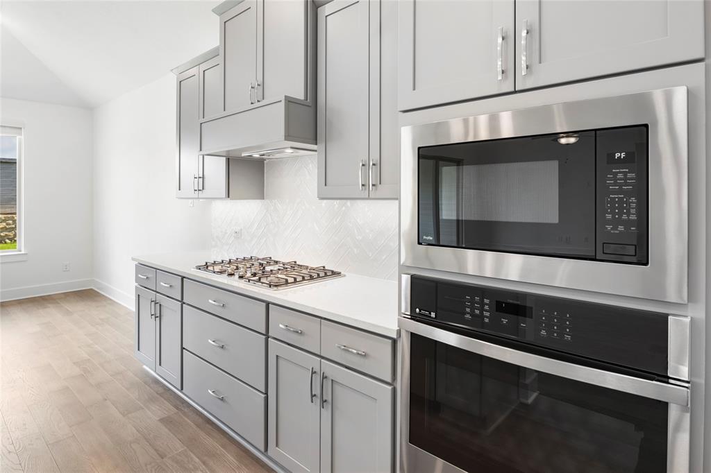 2900 Barbary Road McKinney, TX 75071 - Photo 11 of 36 Contemporary kitchen featuring light gray cabinetry, stainless steel appliances, a gas cooktop, white countertops, and a distinctive patterned backsplash
