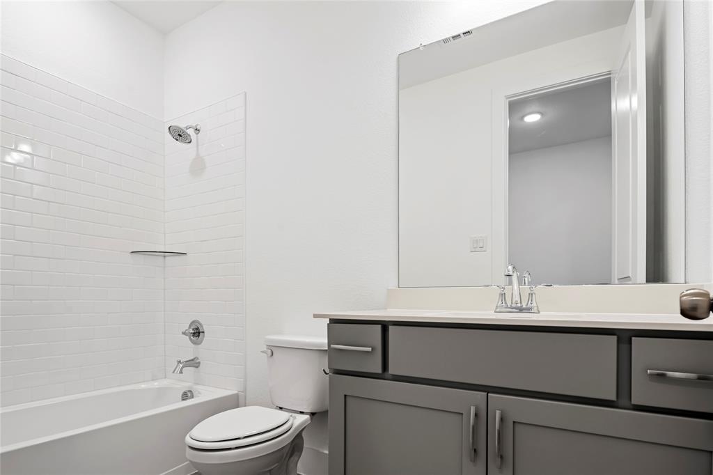 2900 Barbary Road McKinney, TX 75071 - Photo 30 of 36 Contemporary bathroom featuring a white subway tile tub surround, a chrome shower head, a white bathtub, a toilet, and a grey vanity with a light-toned countertop and chrome hardware