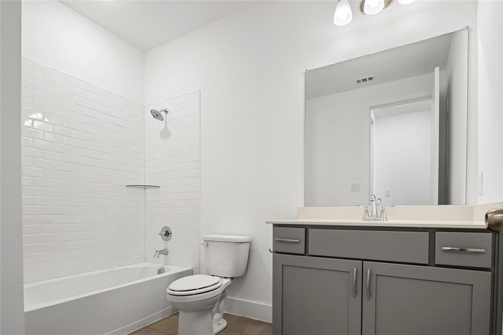 2900 Barbary Road McKinney, TX 75071 - Photo 32 of 36 Modern bathroom featuring a white subway tile tub surround, chrome fixtures, a light-colored vanity countertop, gray cabinetry with brushed nickel hardware, and a large wall-mounted mirror