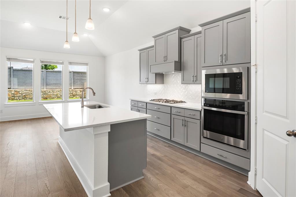 2900 Barbary Road McKinney, TX 75071 - Photo 9 of 36 Contemporary kitchen featuring light wood-finish flooring, an island with an undermount sink and gooseneck faucet, light grey cabinetry, stainless steel appliances, and a gas range
