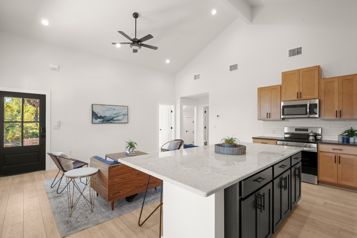 18208 Gregg Bluff Road Jonestown, TX 78645 - Photo 4 of 28 Kitchen with a kitchen bar, stainless steel appliances, dark stone counters, backsplash, and light wood-type flooring