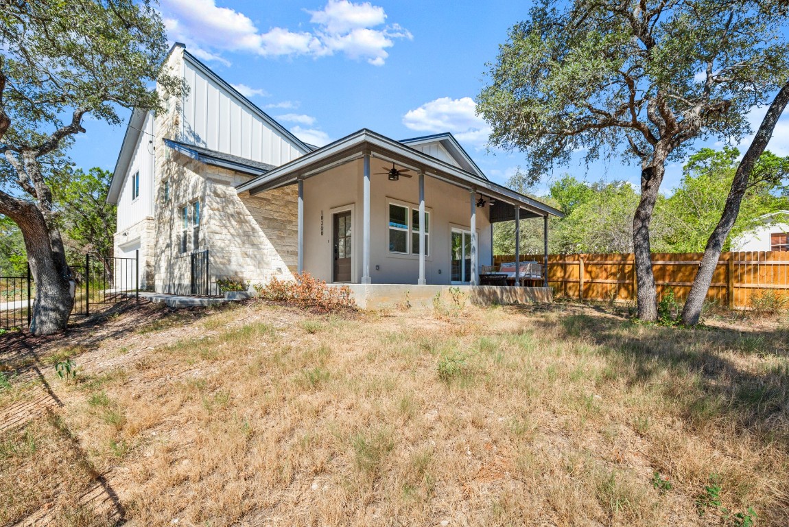 18208 Gregg Bluff Road Jonestown, TX 78645 - Photo 6 of 28 Back of property featuring a ceiling fan, a fenced backyard, a patio, and stone siding