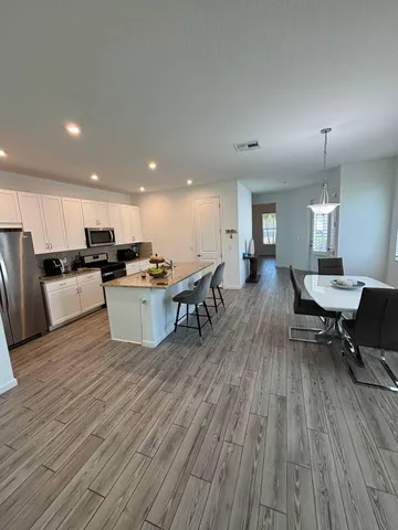 a living room with stainless steel appliances furniture wooden floor and a kitchen view