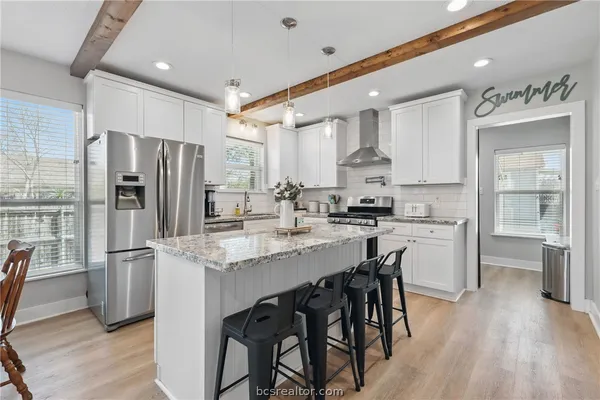 a kitchen with stainless steel appliances granite countertop a refrigerator a sink dishwasher a stove and white cabinets with wooden floor