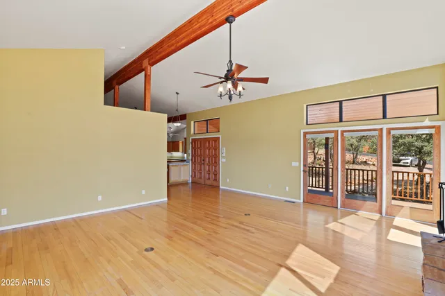 an empty room with wooden floor and way to kitchen