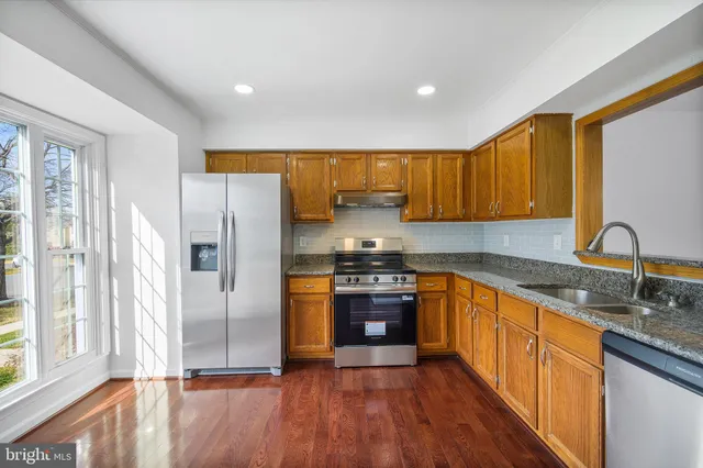 a kitchen with stainless steel appliances granite countertop a refrigerator a sink dishwasher a stove with wooden cabinets and floor