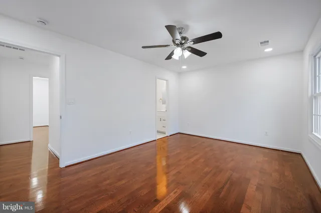 a view of an empty room with wooden floor and a ceiling fan