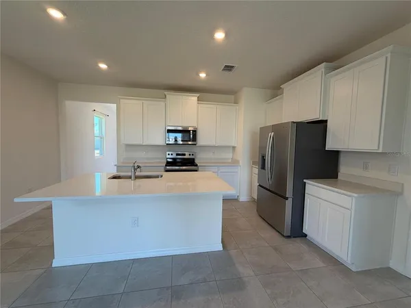 a large kitchen with stainless steel appliances a refrigerator a stove a sink a center island and couches