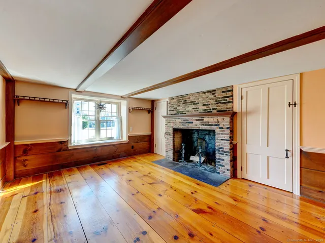 a view of an empty room with wooden floor fireplace and a window